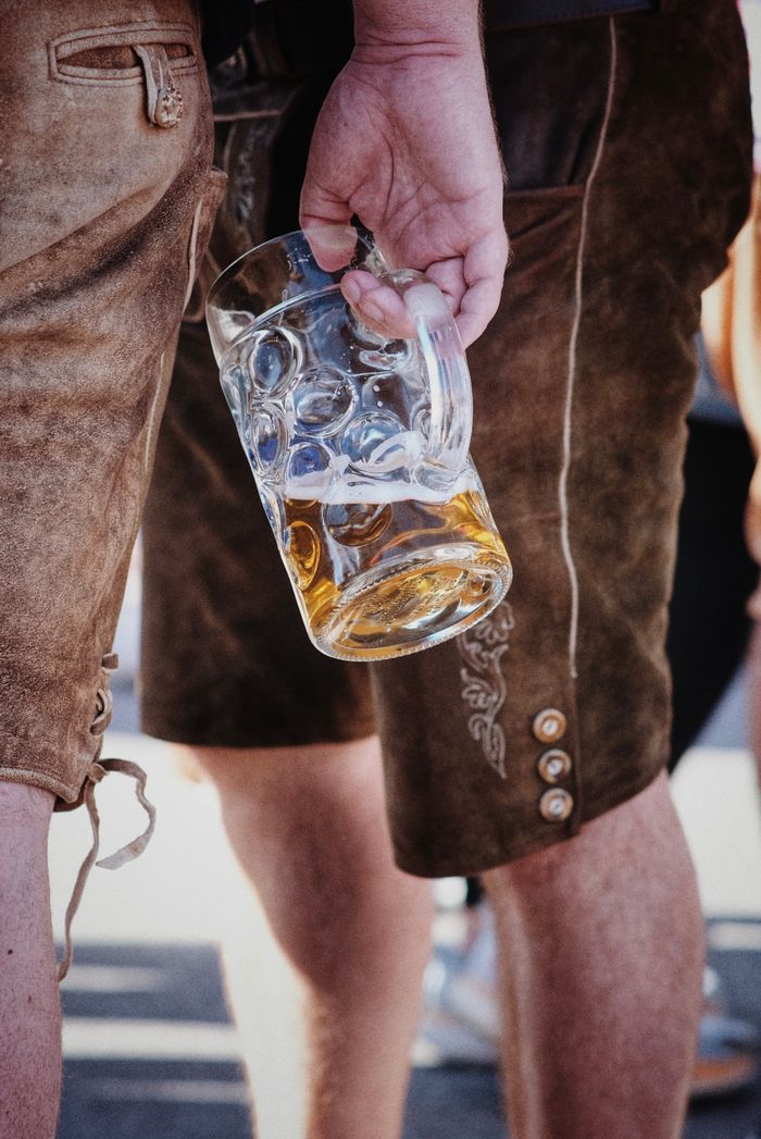 Close-up of a man in lederhosen holding a beer stein outdoors during a festival.