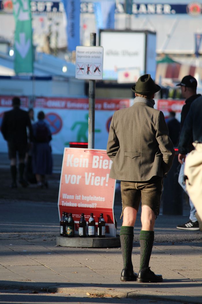 Man in traditional Bavarian attire at Oktoberfest, Munich, standing near a beer sign.