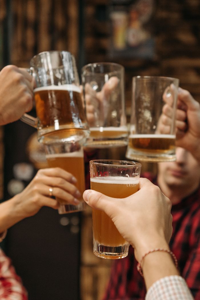 Group of friends clinking beer mugs, enjoying a fun gathering indoors.