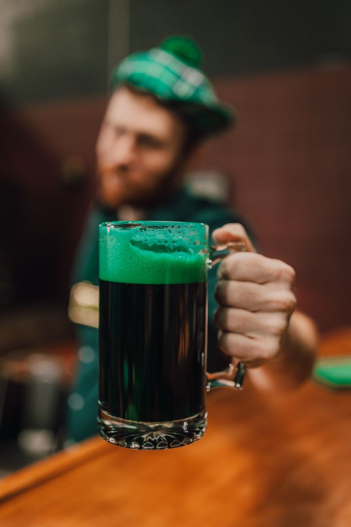 Close-up of a festive green beer mug held up for St. Patrick's Day celebration at an indoor bar.